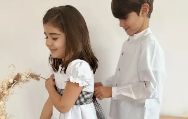 Hermanos de comunión, un niño ayuda a su hermana a ajustar el lazo de su vestido blanco, preparándose para un día especial.
