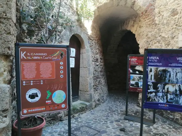 Cartello informativo sul Cammino Calabria Coast to Coast, con scorci di antiche costruzioni in pietra.