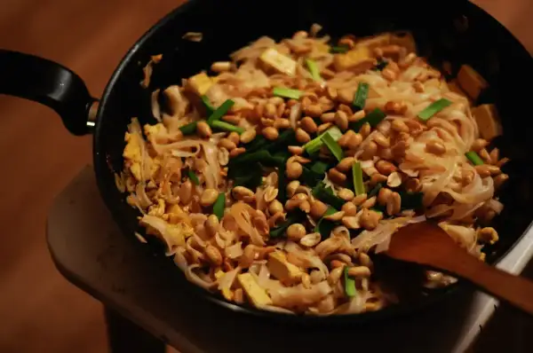 Pyszny sos pad thai z makaronem ryżowym, tofu, orzeszkami ziemnymi i szczypiorkiem, przygotowywany na patelni.