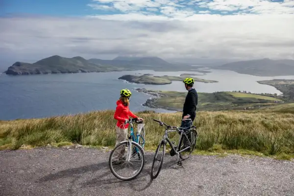 Pareja disfrutando de un paseo en bicicleta por la costa de Irlanda, con vistas a islas y montañas.