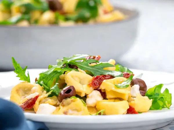 Ein köstlicher italienischer Salat mit Tortellini, Rucola, Oliven und getrockneten Tomaten auf einem Teller.