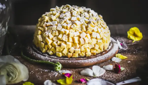 Torta mimosa, una delizia soffice ricoperta di cubetti di pan di Spagna e zucchero a velo, pronta per essere gustata.