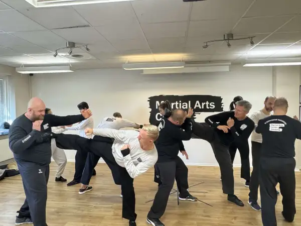 Män tränar wing chun i en lokal. En man utför en hög spark medan andra övar försvar.
