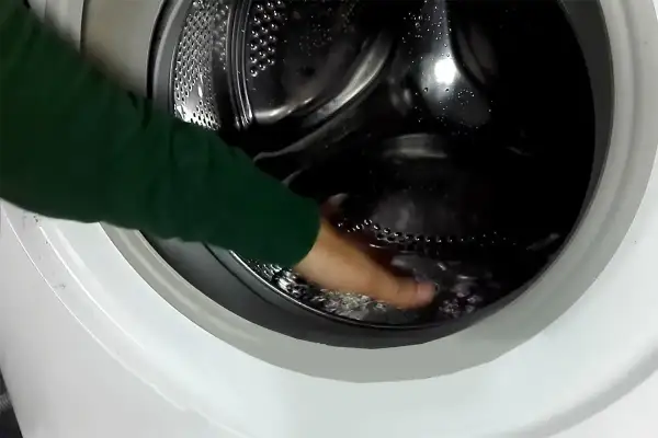 Mano che tocca l'acqua residua nel cestello della lavatrice, un passo per capire come togliere l'acqua dalla lavatrice.