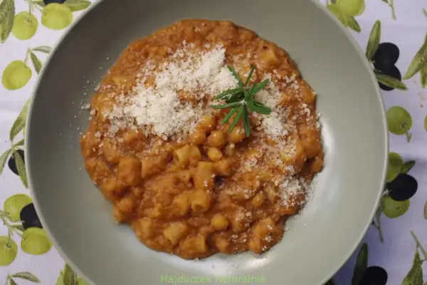 Pyszny makaron z ciecierzycy w sosie pomidorowym, posypany parmezanem i gałązką rozmarynu.