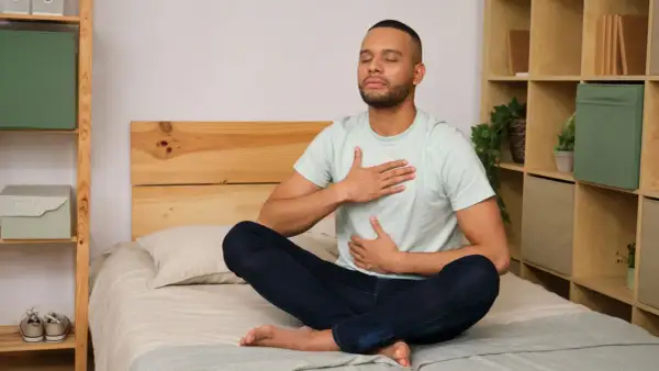 Man meditating on bed, practicing a breathing exercise to fall asleep in 60 seconds.