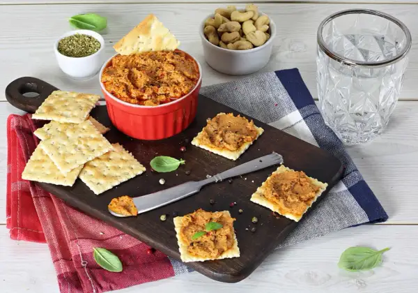 Pasta z suszonych pomidorów na krakersach, podana na desce z dodatkami.