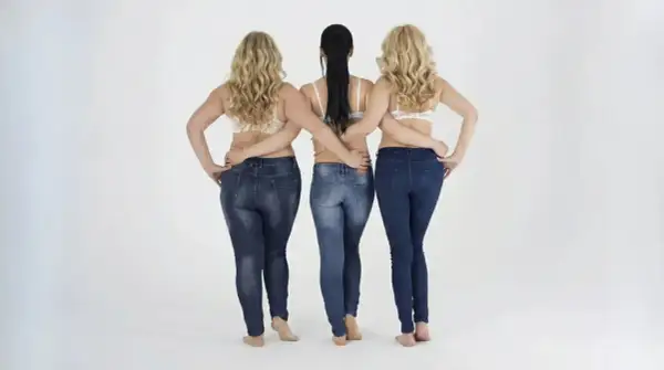 Tre donne in jeans, una con fisico a pera uomo, mostrano diverse forme del corpo.