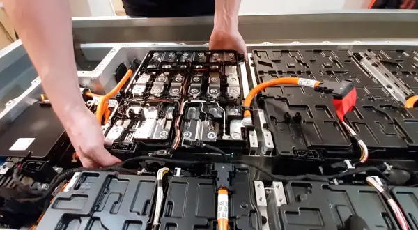 Manos trabajando en el interior de un paquete de baterías de coche eléctrico. Averiguar cuanto cuesta cambiar la bateria del coche es clave.