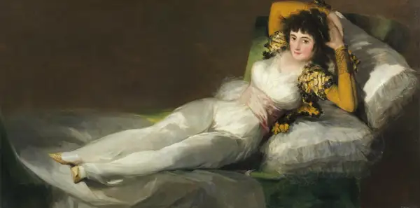 La venus del espejo, una mujer recostada en un diván, viste un traje blanco y mira al espectador con una expresión seductora.