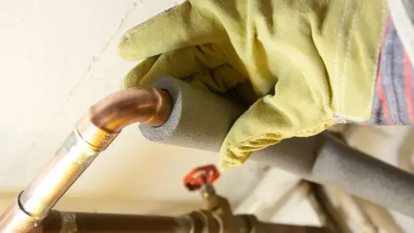 Mit gelben Handschuhen werden Heizungsrohre isoliert, um Energie zu sparen.