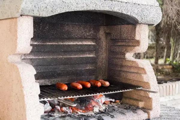 Prosty murowany grill z cegły, na którym pieką się kiełbaski nad żarem.