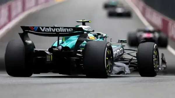 Un coche Aston Martin F1 verde compite en la pista, con otros coches borrosos detrás.