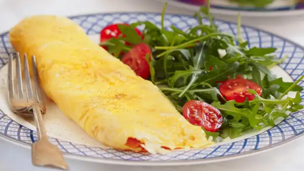 Tortilla francesa rellena, dorada y esponjosa, servida con una fresca ensalada de rúcula y tomates cherry. Un bocado delicioso y saludable.