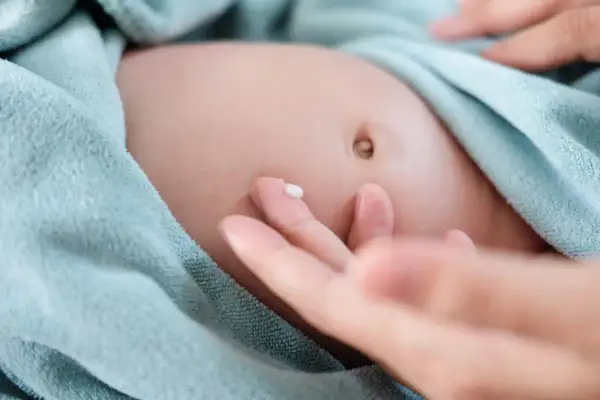 Delikatna skóra niemowlaka, pępek i kropla kremu na palcu. Tak wygląda pielęgnacja, która może pomóc w przypadku przepukliny pępkowej.