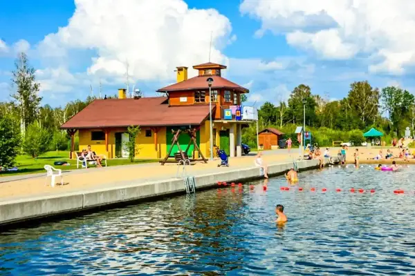 Słoneczny dzień nad jeziorem w Węgorzewie. Rodziny odpoczywają na plaży, dzieci kąpią się w wodzie. Idealne miejsce na wakacje z rodziną, oferujące wiele atrakcji dla dzieci.