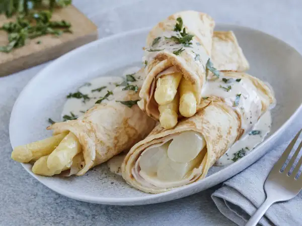 Pfannkuchen mit Spargel und Schinken, übergossen mit einer cremigen Sauce und garniert mit Petersilie.