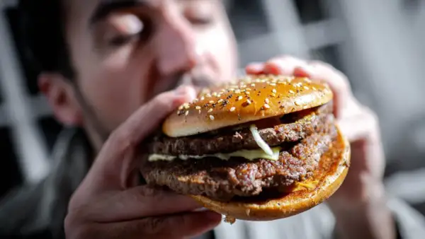 Mann hält einen saftigen Doppel-Cheeseburger mit Sesambrötchen. Perfekt für Burger Rezept Ideen!