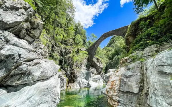 Idyllische Schlucht mit Steinbrücke, ideal für Tessin Wandern. Türkisgrünes Wasser fließt zwischen Felsen.