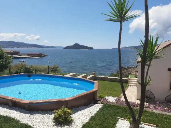 Piscina azul con vistas al mar y a la playa de Limens. Palmeras y césped verde rodean la zona de descanso.
