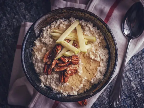 Porridge zubereiten: Cremiger Haferbrei mit Apfelspalten, Pekannüssen und Honig in einer Schüssel, daneben ein Löffel.