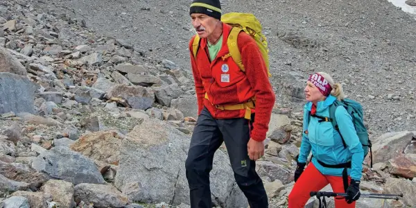 Simon Gietl und eine Frau wandern auf einem felsigen Berghang. Sie tragen Rucksäcke und Wanderkleidung.