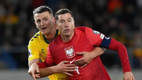 Robert Lewandowski, kapitan Polski, w czerwonej koszulce z orłem, walczy o piłkę z przeciwnikiem.