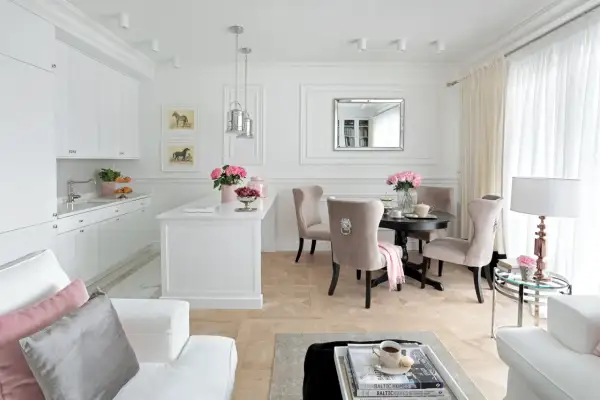 Elegancki salon z kuchnią inspiracje: białe meble, beżowe krzesła, okrągły stół, lustro, obrazy z końmi, kwiaty.