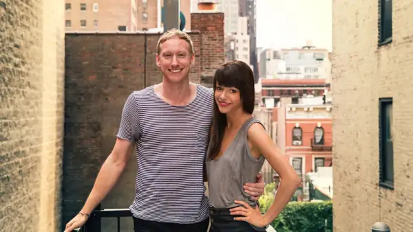 Jessica Walsh and her partner, perhaps celebrating a milestone in her most famous work, stand on a rooftop with a city skyline behind them.