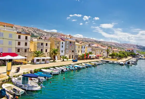 En kuststad i Kroatien med färgglada hus, en hamn full av båtar och en bergig bakgrund. Här finns fakta om Kroatien.