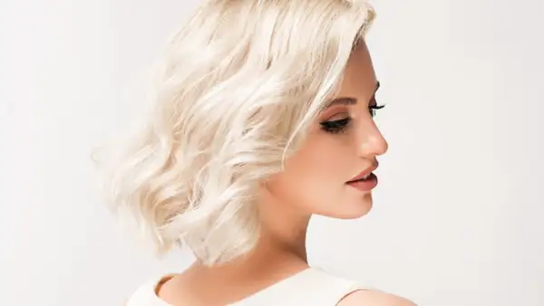 Kobieta z krótkimi, blond falowanymi włosami i makijażem.