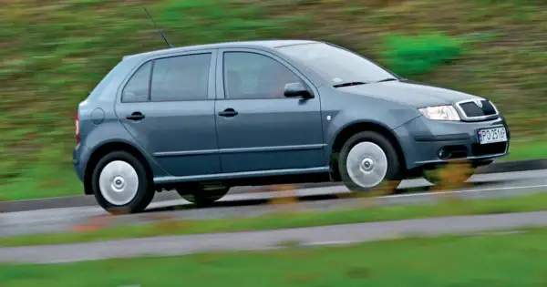 Szara, nowa Skoda Fabia pędzi po mokrej drodze, rozmazując zielone tło.
