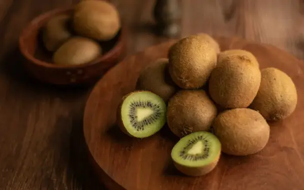 Kiwi, noti per essere tra i cibi che fanno andare in bagno, sono disposti su un tagliere di legno. Uno è tagliato a metà, mostrando la polpa verde e i semi neri.