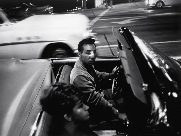 Garry Winogrand uchwycił nocną jazdę kabrioletem. Mężczyzna za kierownicą, kobieta obok. Rozmyte światła miasta.