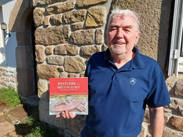 Un homme souriant tient un livre sur l'histoire du breton écrit. Son nom de famille breton est Favreau.