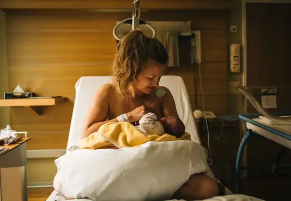 Nybliven mamma ammar sitt barn på en sjukhussäng. En lugn stund efter förlossningen, kanske inför en efterkontroll på MVC.