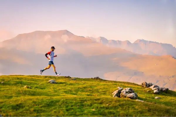 Un coureur en plein effort sur un sentier de montagne, prêt pour une ultra trail distance. Le soleil couchant illumine le paysage.