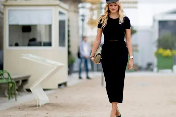 Elegancka kobieta w czarnej sukience i kaszkiecie, niosąca kopertówkę. Idealna stylizacja, gdy zastanawiasz się, co na wierzch do czarnej sukienki.