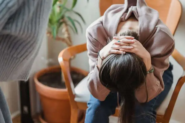 En person sitter med huvudet i händerna, ser ut att må dåligt. Kanske upplever hen biverkningar av något.