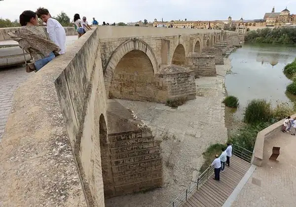 Gente admira el puente romano de Córdoba. Para llegar, sigue el río Guadalquivir.