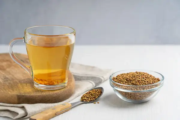 Glas mit Bockshornklee-Tee und Samen daneben. Informieren Sie sich über mögliche bockshornklee nebenwirkungen, bevor Sie ihn konsumieren.