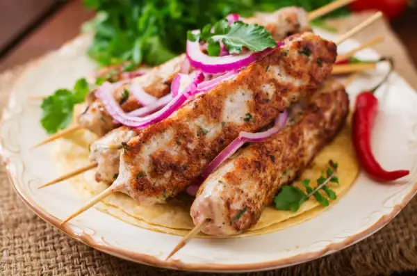 Aksamitny kebab z indyka na talerzu, ozdobiony krążkami czerwonej cebuli i świeżą natką pietruszki. Obok leży pikantna papryczka chili.