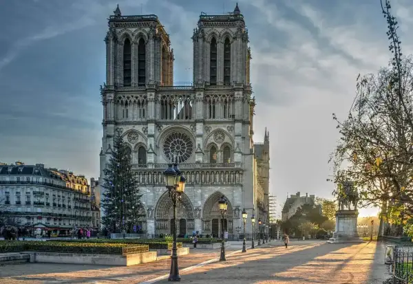 La maestosa cattedrale di Notre Dame de Paris, con le sue torri imponenti e un albero di Natale illuminato, si erge maestosa sotto un cielo nuvoloso.
