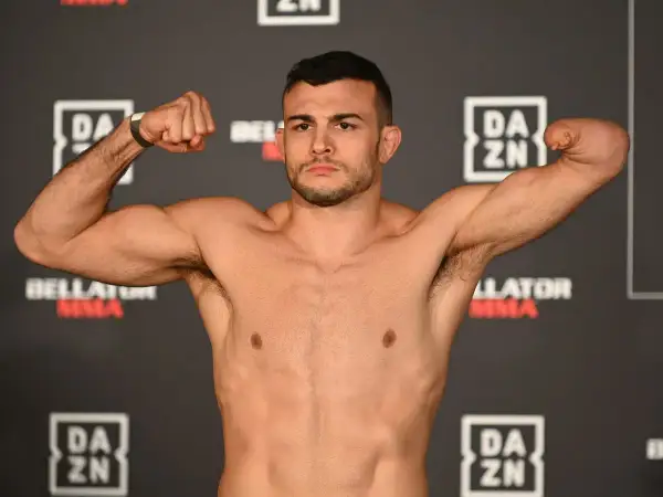 Fighter with one arm boxing, flexing his bicep. He stands against a backdrop of DAZN and Bellator MMA logos.