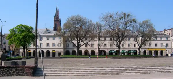 Łódź stare miasto: plac z kamiennymi schodami, arkadowymi budynkami i wieżą kościelną w tle.