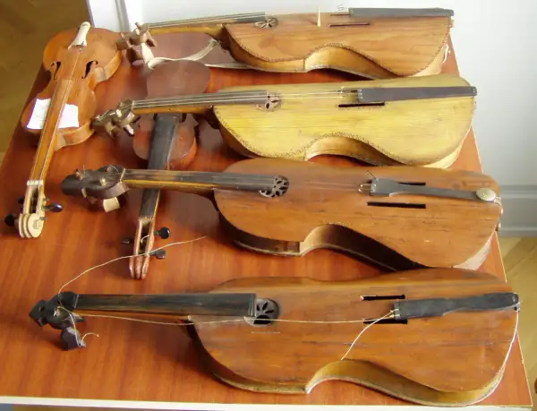 Kilka drewnianych instrumentów smyczkowych, w tym skrzypce, leżących na drewnianym stole.