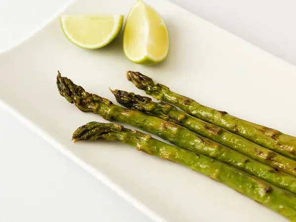 Asperges rôties sur une assiette blanche avec des quartiers de citron vert. Une idée simple pour une recette d'asperges savoureuse.