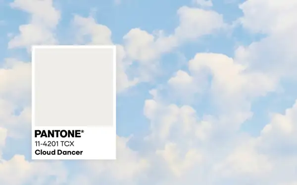 Pantone-Farbkarte "Cloud Dancer" vor einem Himmel mit Wolken. Diese zarte Farbe könnte die Farbe des Jahres 2026 sein.