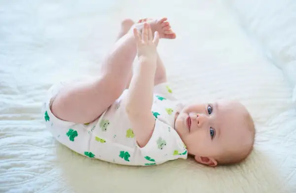 Ein Baby mit 6 Monaten kann schon viel! Dieses Baby liegt auf dem Rücken, hebt seine Beine und spielt mit seinen Füßen.
