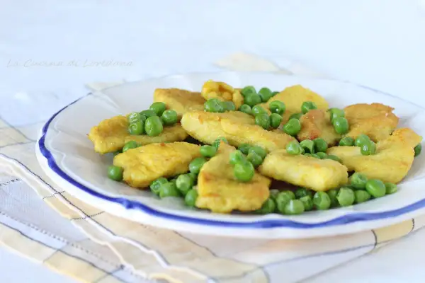 Petto di pollo impanato e dorato, servito con piselli freschi su un piatto bianco bordato di blu.